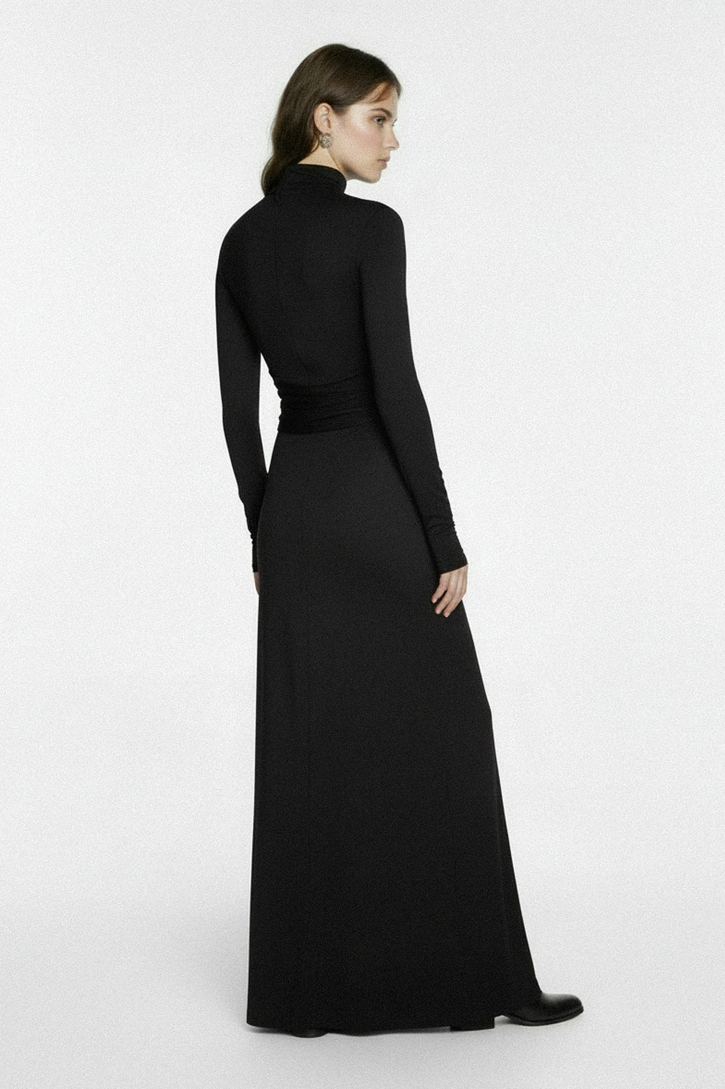 Woman wearing a black long-sleeve  jersey gown on a white background, made from sustainable fabric, by independent designer based in London, in timeless style, quiet luxury