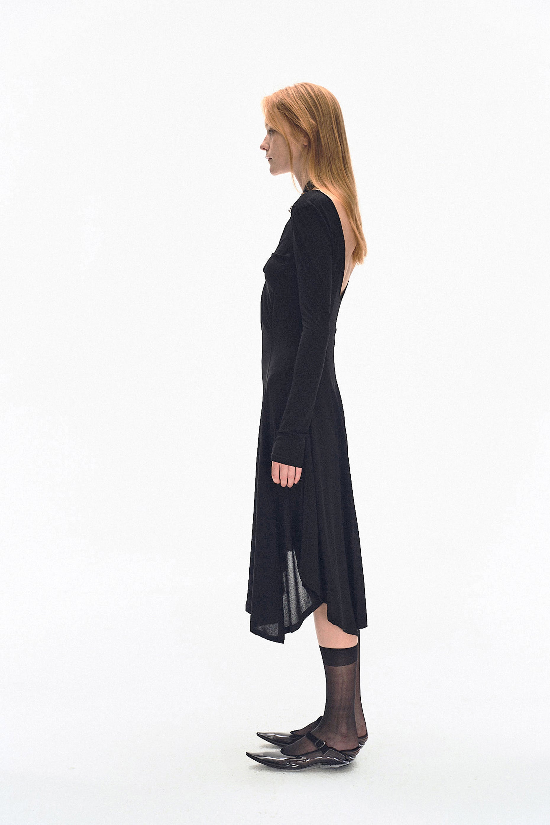 Model wearing YIBRI black long sleeve fitted knit dress with deep V-neck and twisted front draping — modern quiet luxury silhouette.
