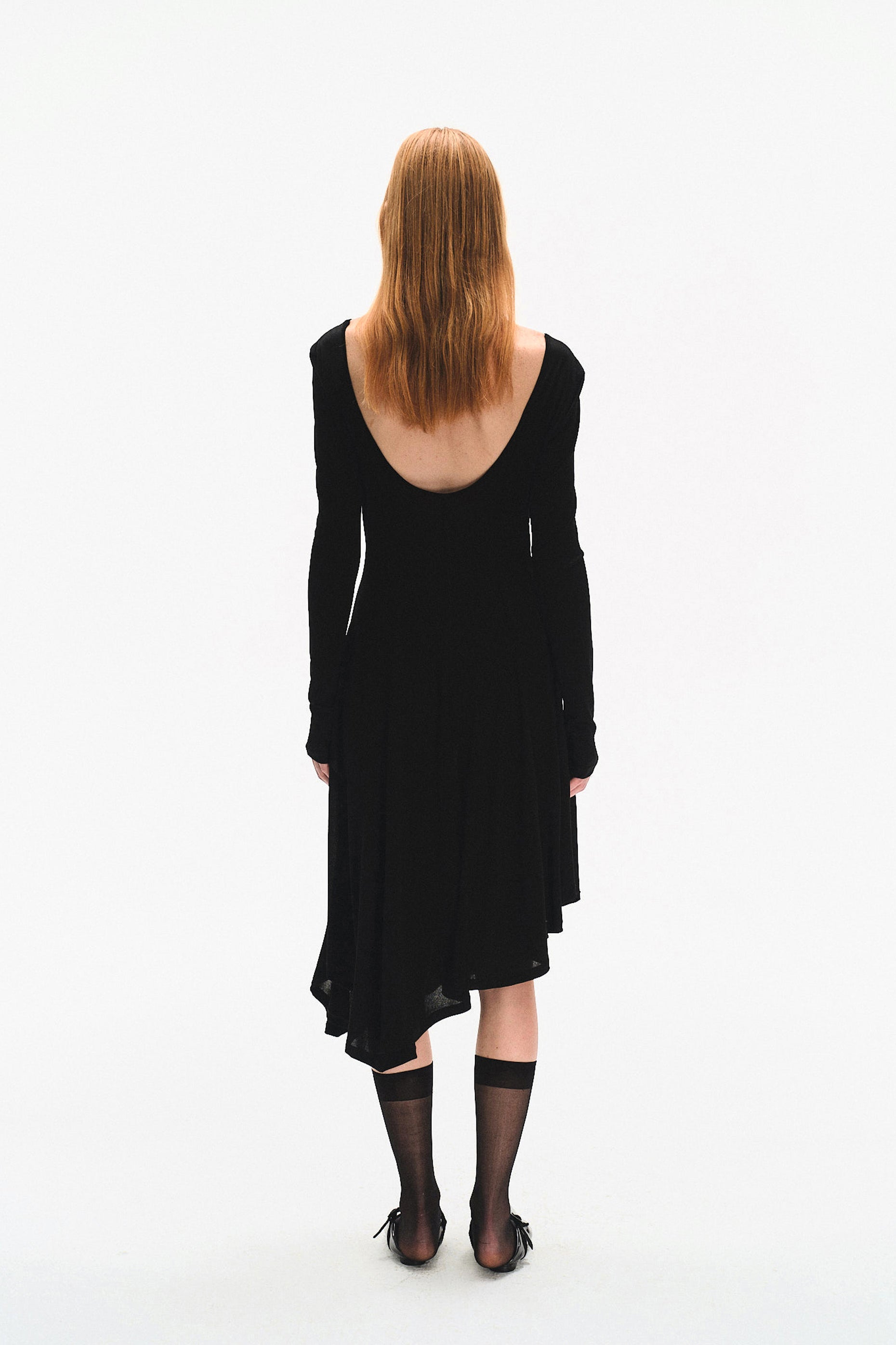 Side profile of model in YIBRI black long sleeve fitted knit dress showcasing sculpted bodice, twisted drape detail and quiet luxury elegance.