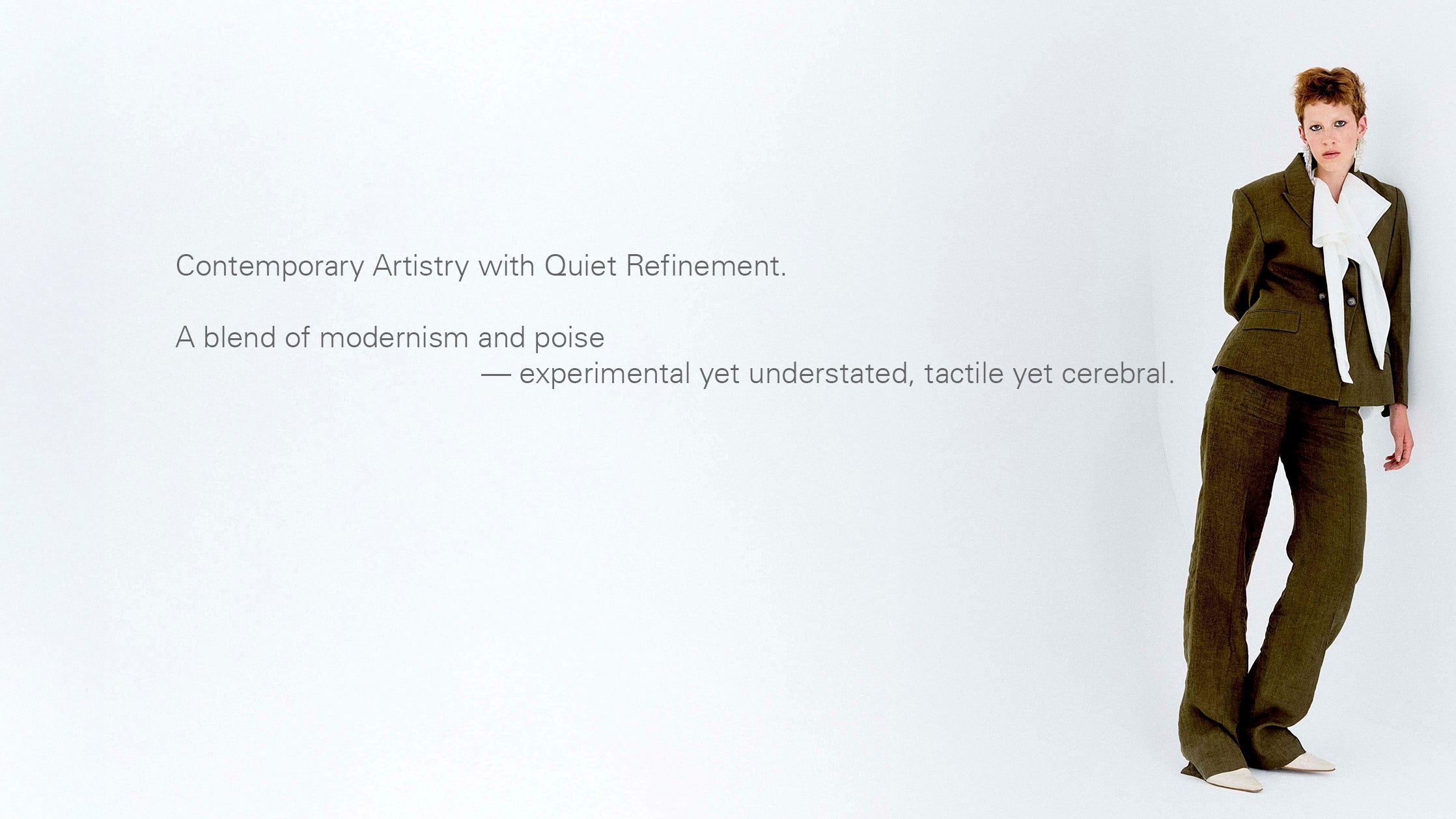 a women in yarn dyed moss green suit leaning against the white wall, the texts write contemporary artistry with quiet refinement. a blend of modernism and poise, experimental yet understood, tactile yet cerebral