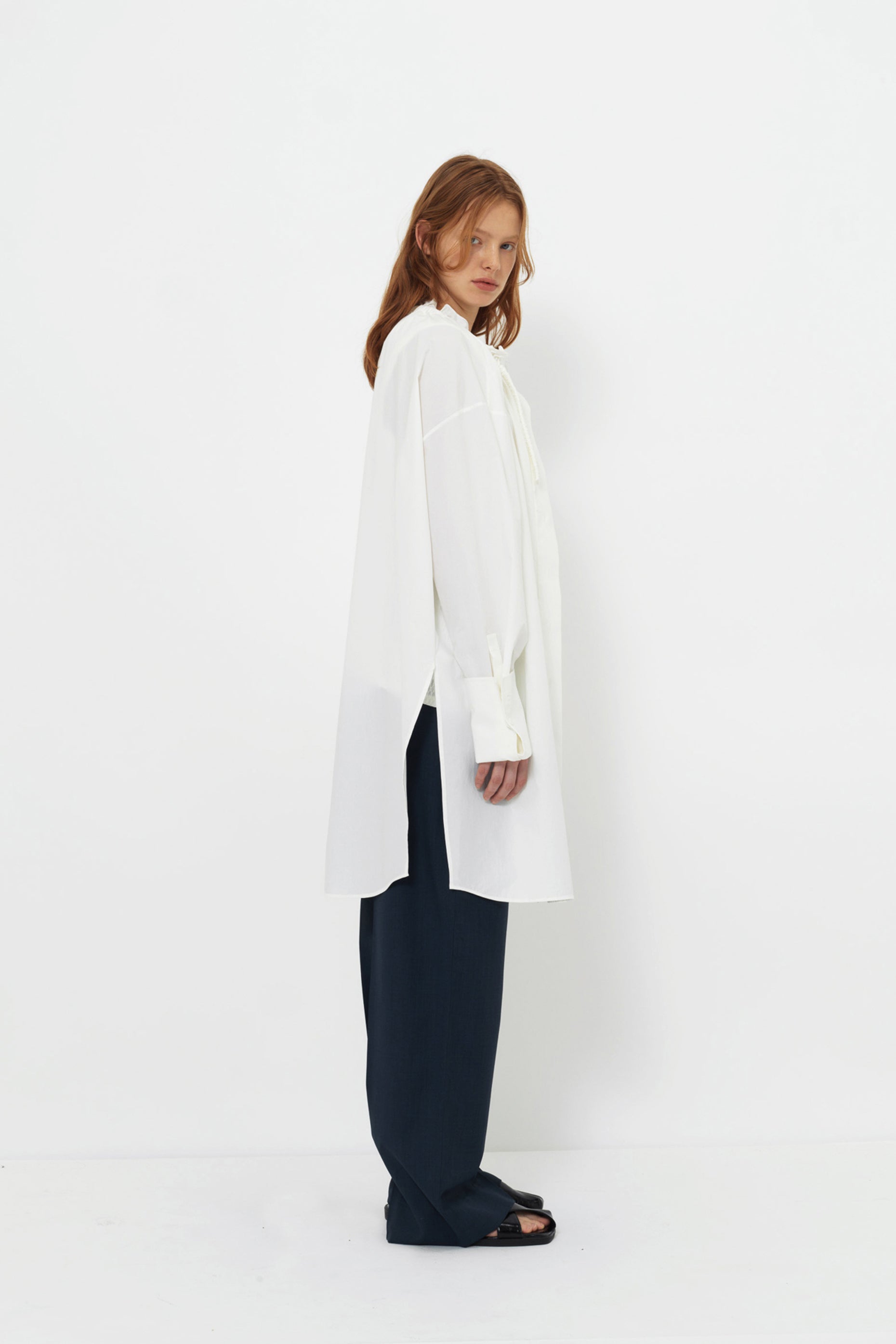 Side view of model in the YIBRI Ruched Collar Long Shirt in white washed cotton, showing extended hem, clean drape and gathered neckline.