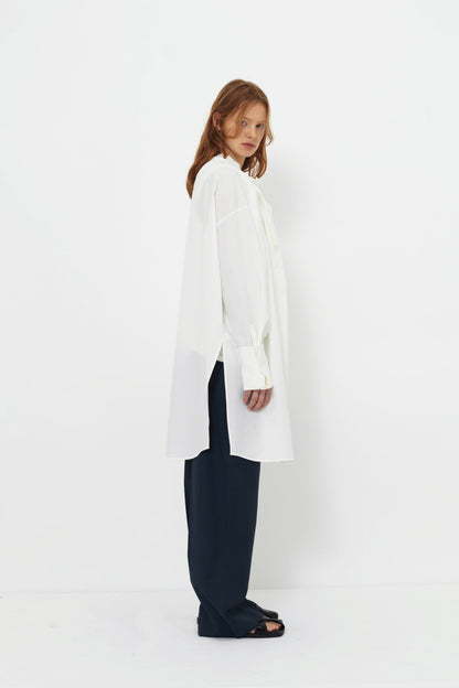 Side view of model in the YIBRI Ruched Collar Long Shirt in white washed cotton, showing extended hem, clean drape and gathered neckline.