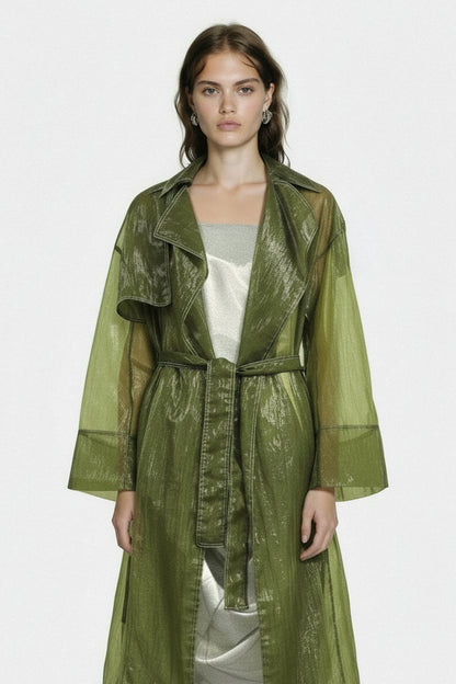 Woman wearing a green trench coat over a white top on a light gray background