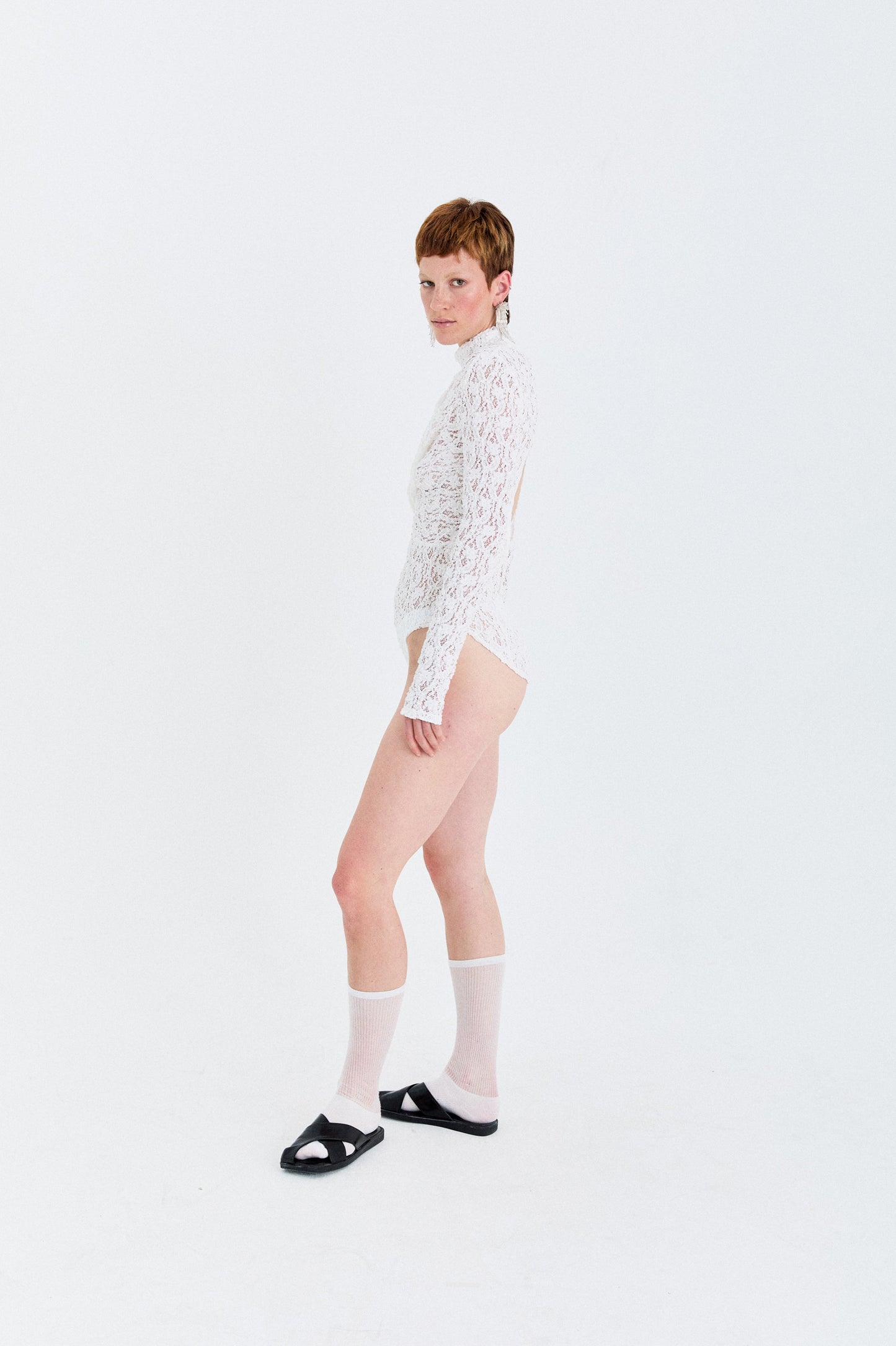 Model dynamic pose in the YIBRI Reversible Twisted-Knot Top in white lace (reverse colourway), showing the sculptural twist and sheer floral lace texture.