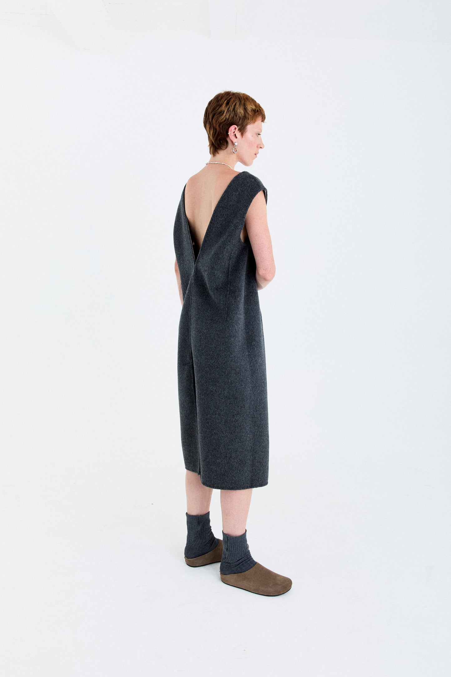 Woman wearing a dark grey dress with a back cutout on a white background, timeless style, quiet luxury by independent designer based in London 