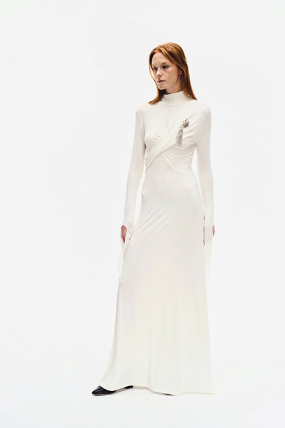 Side angle of YIBRI ivory long-sleeve maxi dress featuring soft draping, high neckline and sculptural wrap detail with silver brooch ornament